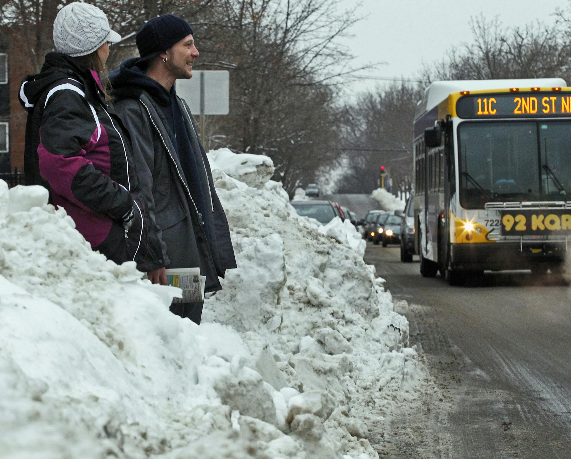 MARLIN LEVISON*mlevison@startribune.com GENERAL INFORMATION : ]¬†Pedestrians fighting the large mounds of snow piled up on urban street corners as a result of the resent snow storms. IN THIS PHOTO: Amy Smith, left and Scott Johnson waited in the middle of a snow pile for a metro bus on Franklin Ave. ORG XMIT: MIN2014103017533763