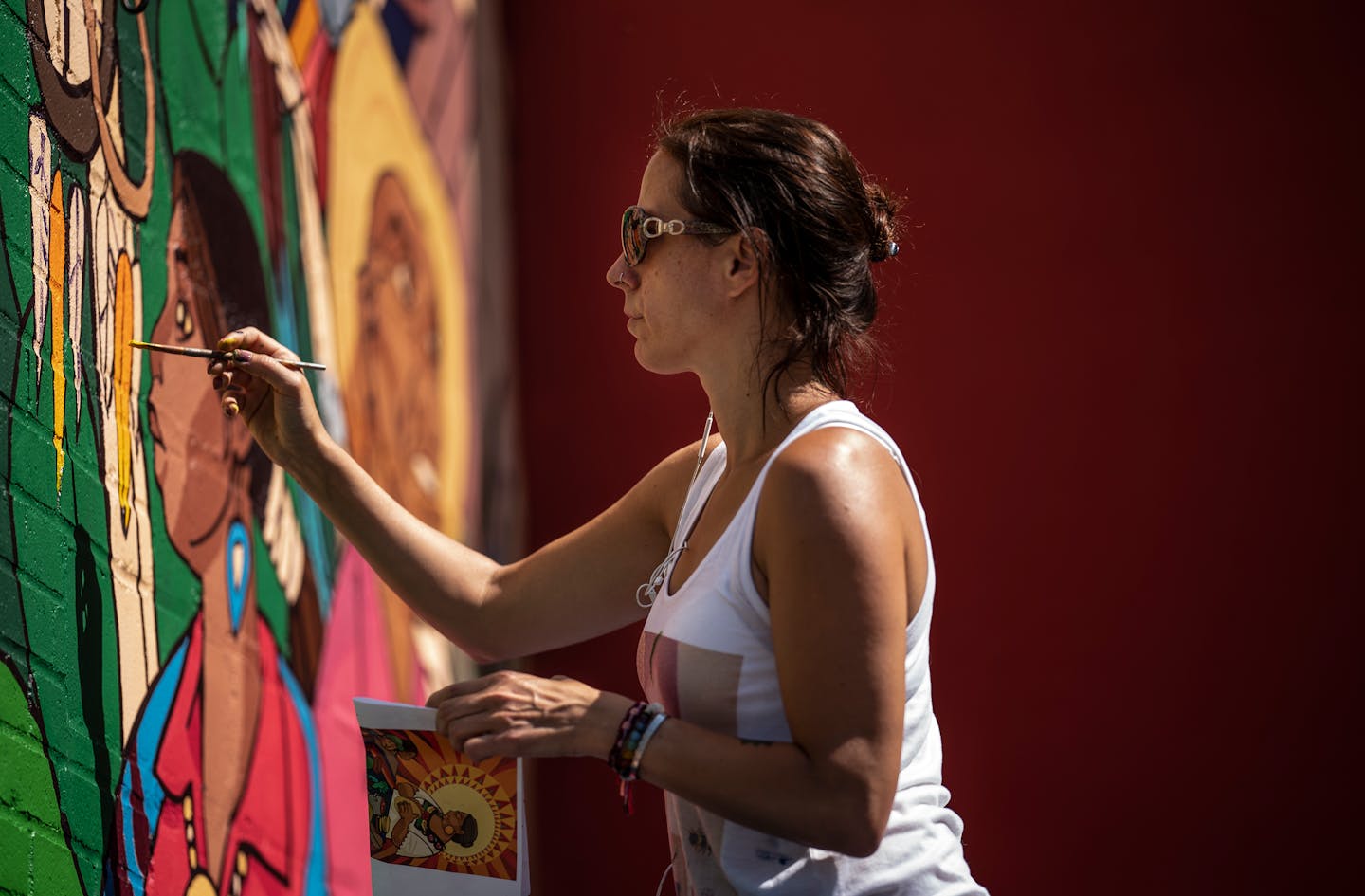 Artist Daniela Bianchini at left, painted a mural called "Legends of Identity" on the outside wall of El Burrito Mercado Monday. The mural was reflected in the window fo the building.] Jerry Holt •Jerry.Holt@startribune.com