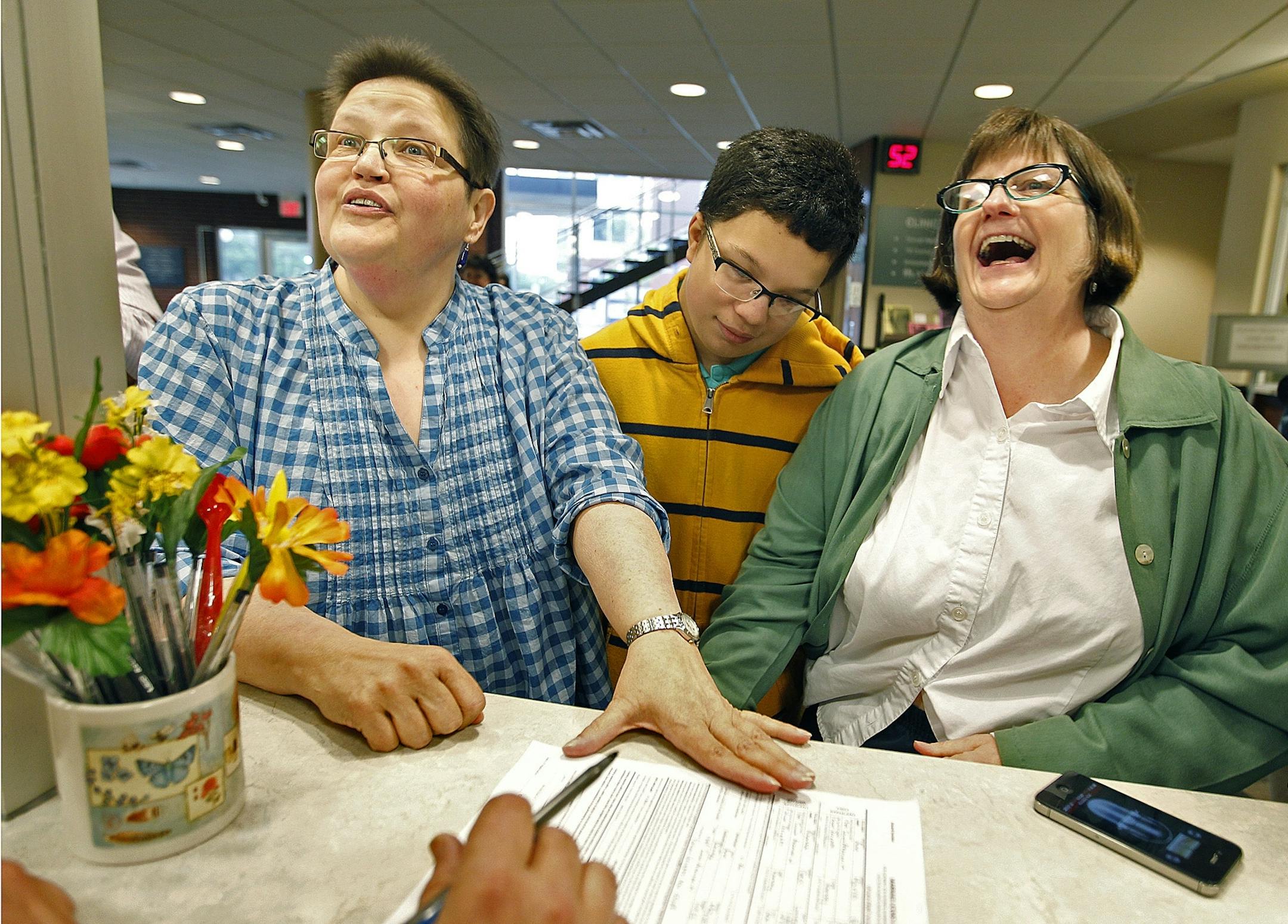 With their son Andy Lundquist, 13, center, as a witness to history, Rhonda Lundquist, left, and Ann Marie deGroot, of Falcon Heights enjoyed a laugh as they were the first couple to apply for a marriage license at the Ramsey County Public Health Center, Thursday, June 6, 2013.