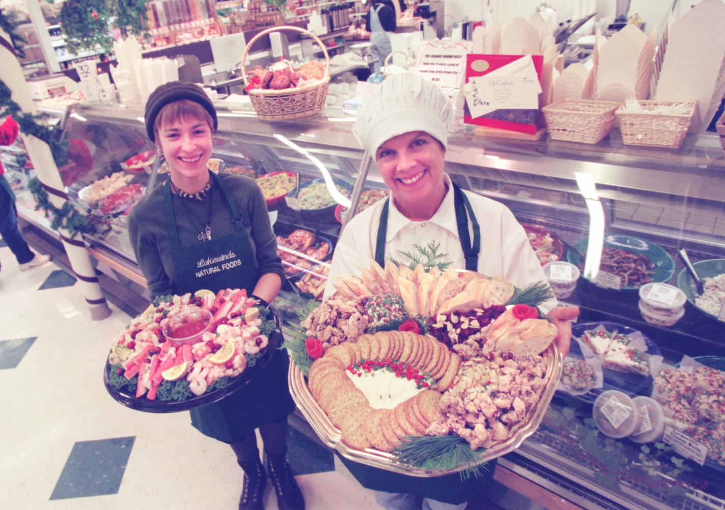 -- Lakewinds Natural Foods head chef Nancy LaLiberte, right, shows off a party platter with fresh sliced bread, gorgonzola cheeze balls, their famous pesto torta and a variety of other dips, spreads and crackers. Counter clerk Addie Motzko, left, shows off a seafood platter from the meat department with shrimp, crablegs and cocktail sauce. Lakewinds deli also serves gourmet sandwiches, a wide selection of imported and domestic cheeze, salads, desserts, pastries and entrees. It is located on 1752