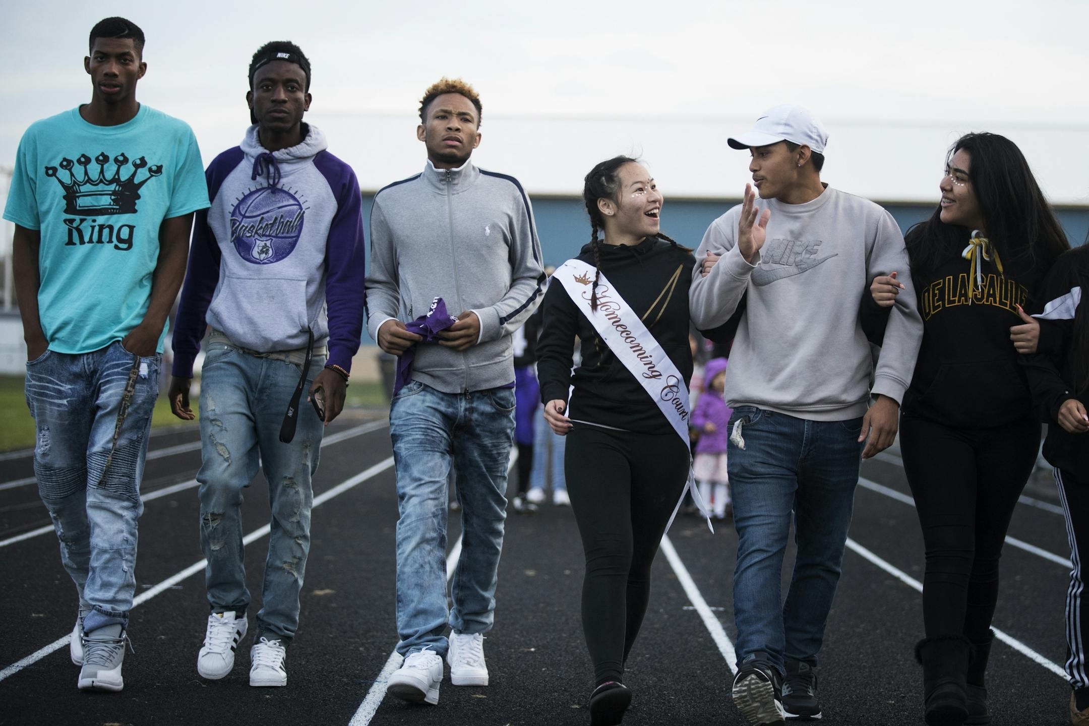 Homecoming court members Annie Vue, center in black is escorted by DeShawn Pickford, center in gray, and other friends during halftime.
