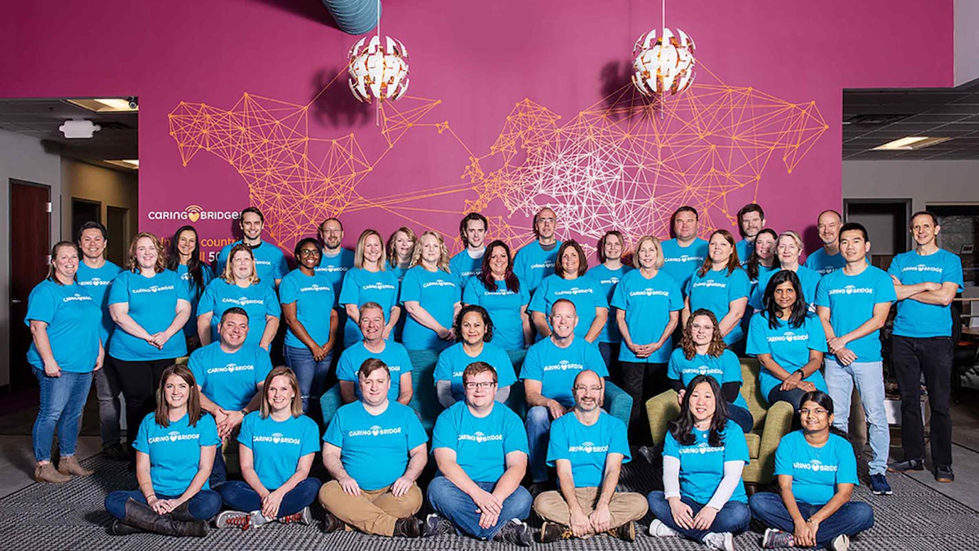 CaringBridge staff in front of a wall map, lit up with places where users have made CaringBridge sites.