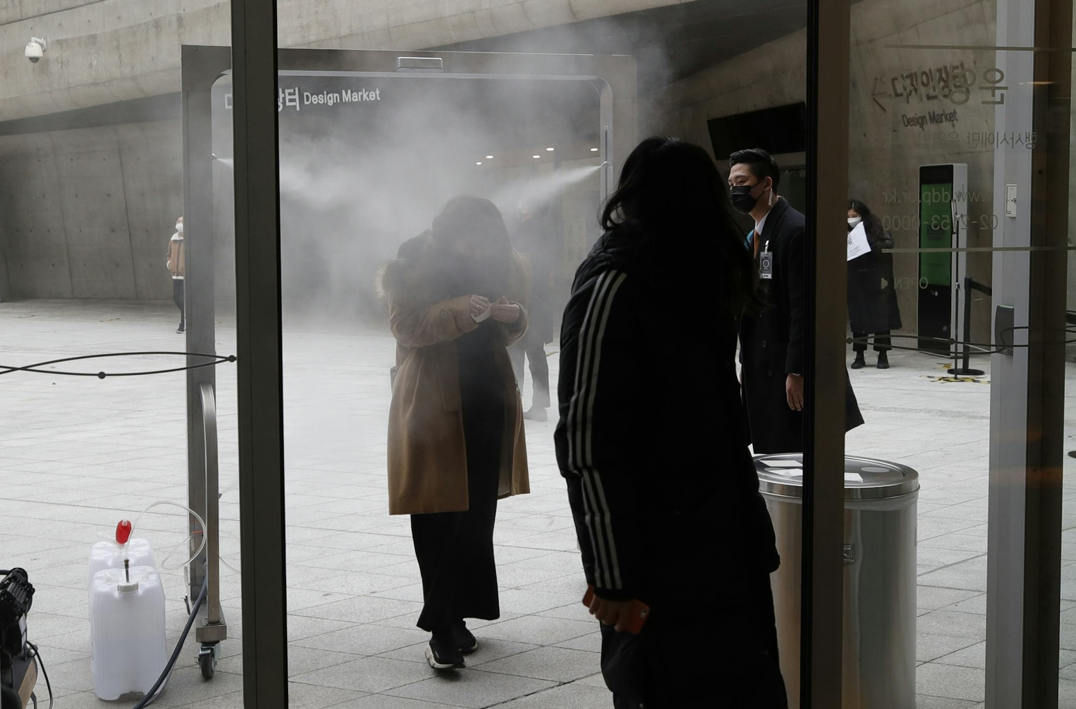 People walk through a gate which sprays disinfectant as a precaution against the coronavirus in front of a venue of K-pop band BTS' press conference in Seoul, South Korea, Friday, Nov. 20, 2020.
