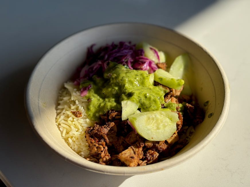 Sumac chicken rice bowl with fresh cucumbers, cabbage and spicy green herb sauce.