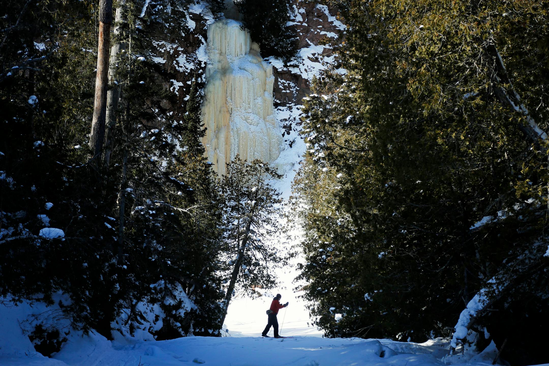 Minnesota State Parks Magazine Story - With an Ice wall, formed from the running water from a small creek as a backdrop, Steve Ramberg skis down the Cascade River at Cascade River State park.