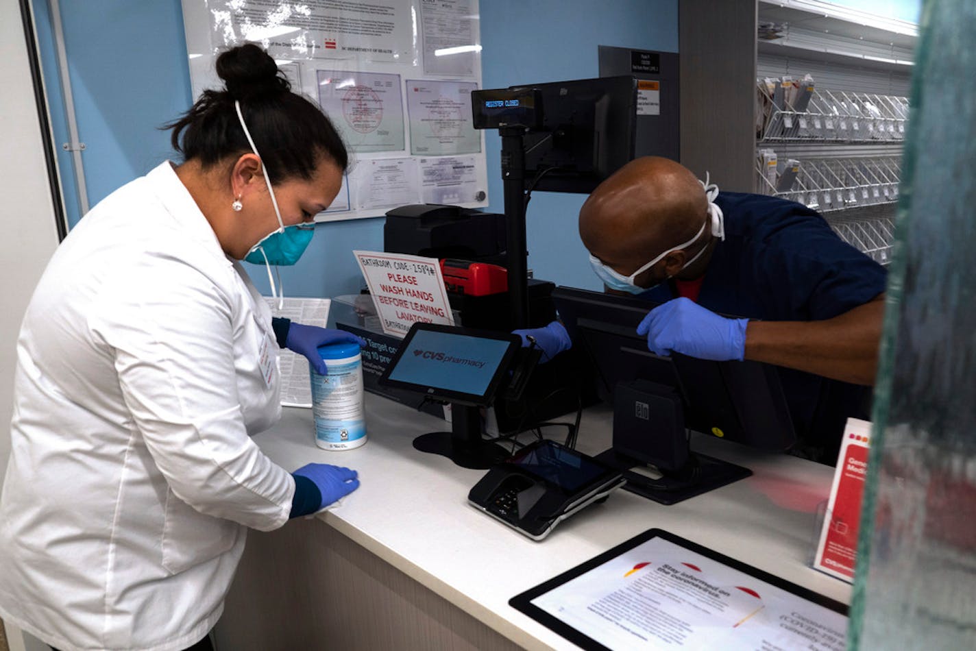 Pharmacist Evelyn Kim and pharmacy technician Omar Toppin clean the counter at the CVS pharmacy at Target in the Tenleytown area of Washington in March. Many businesses are providing or requiring that staffers wear masks or other protective gear.