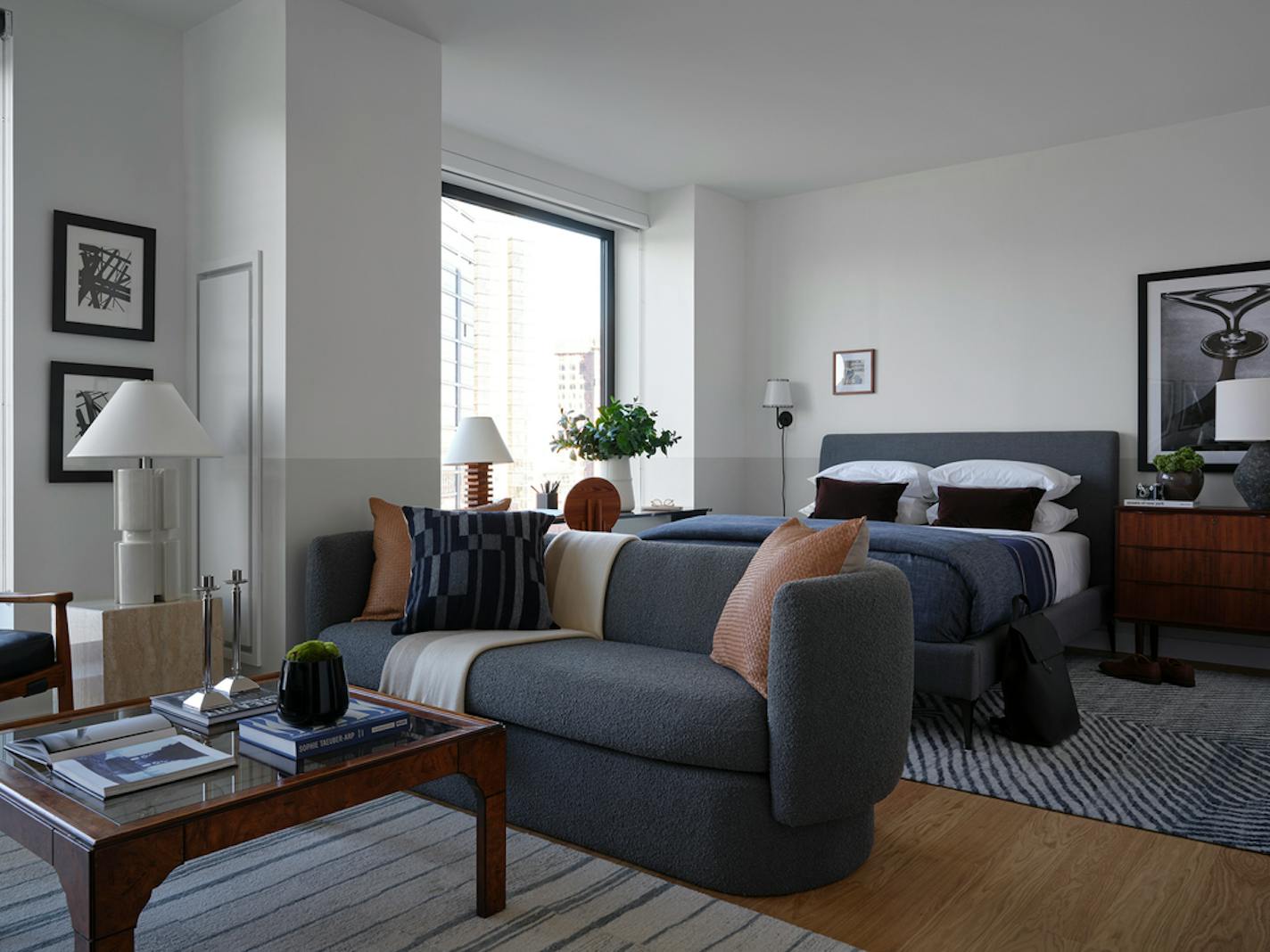 Studio apartment with wood coffee table and gray couch in foreground and bed in background.