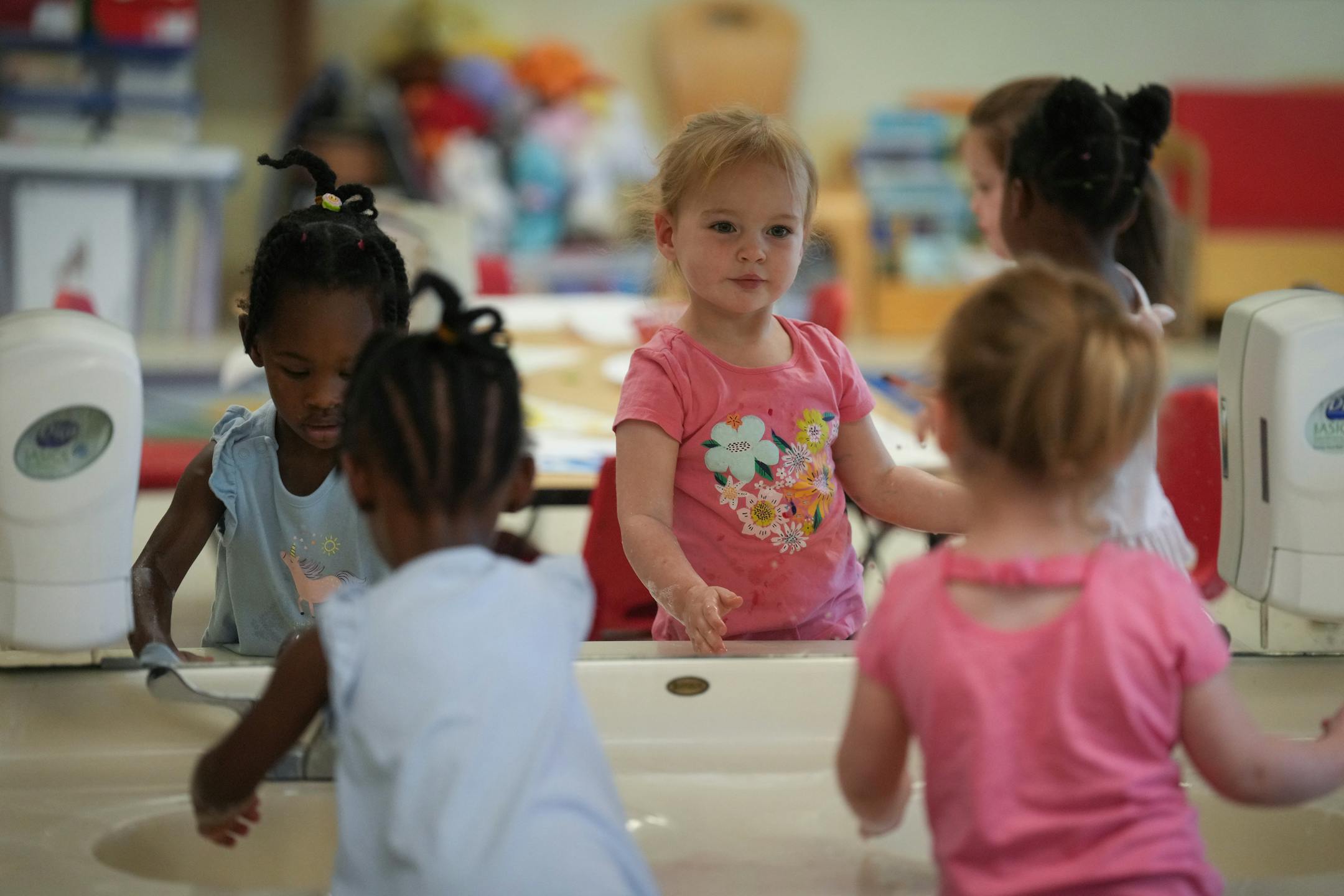 A student catches a glimpse of her reflection after washing her hands next to another student in the class of two-year-olds.
