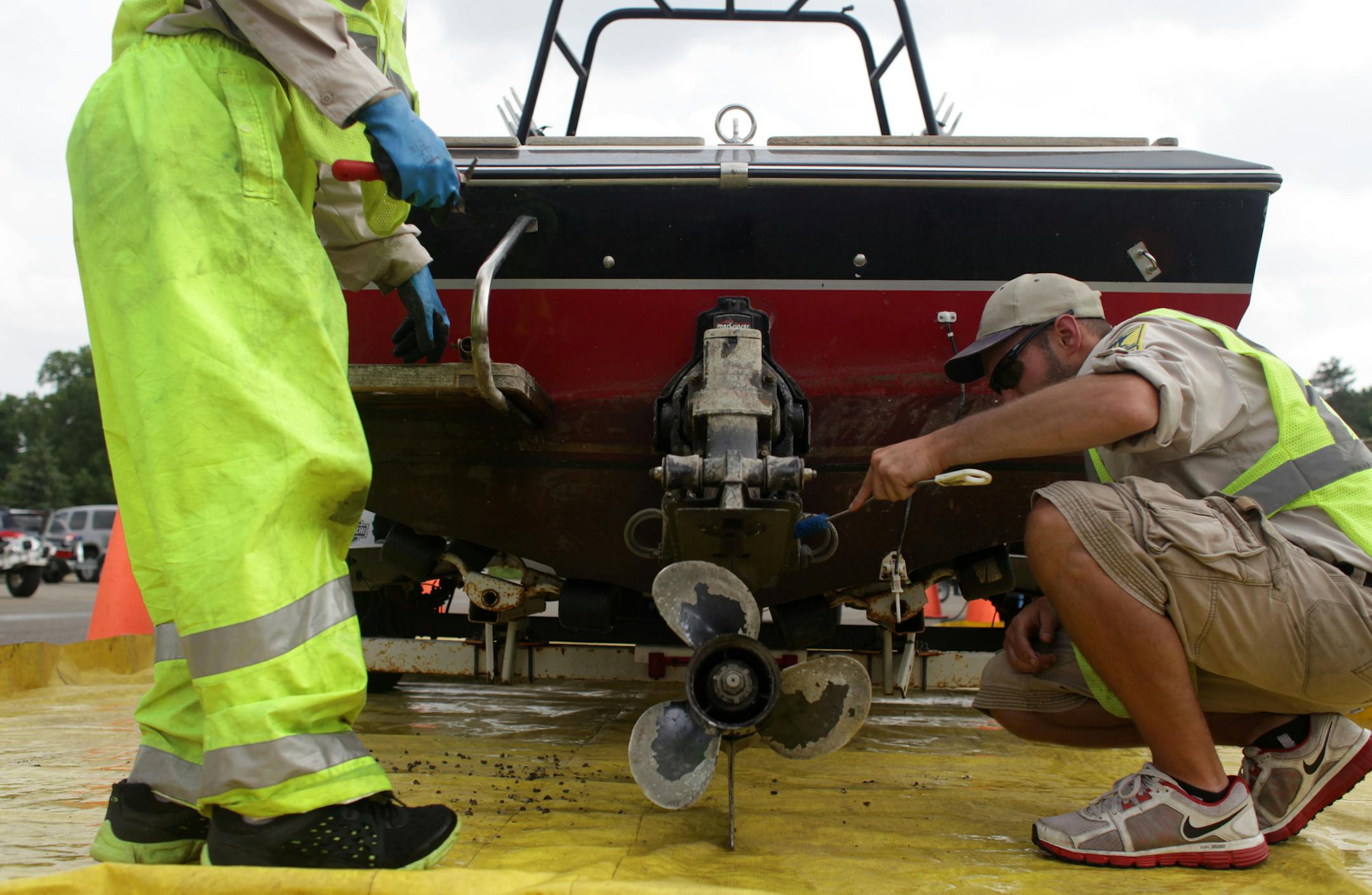 The DNR’s Joe Hale, left, and Ben Troop scrubbed dead zebra mussels off a boat after the owner was fined $300 at Grays Bay boat ramp Thursday.