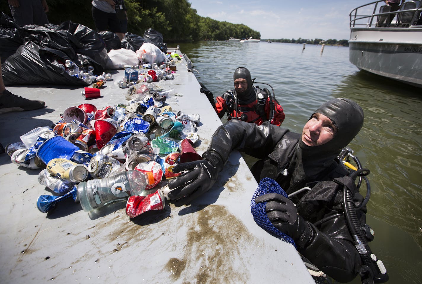 Hennepin County Sheriff's Office divers Rick Rehman, right, and Rich Crosson place trash they've collected in Lake Minnetonka onto a barge. ] (Leila Navidi/Star Tribune) leila.navidi@startribune.com BACKGROUND INFORMATION: Clean up near Big Island on Lake Minnetonka on July 5, 2016. Volunteers are increasing clean-up efforts on Lake Minnetonka after the rowdy July 4th holiday weekend results in boatloads of trash. On Tuesday, Hennepin County Sheriff's Office divers will join the effort for the f