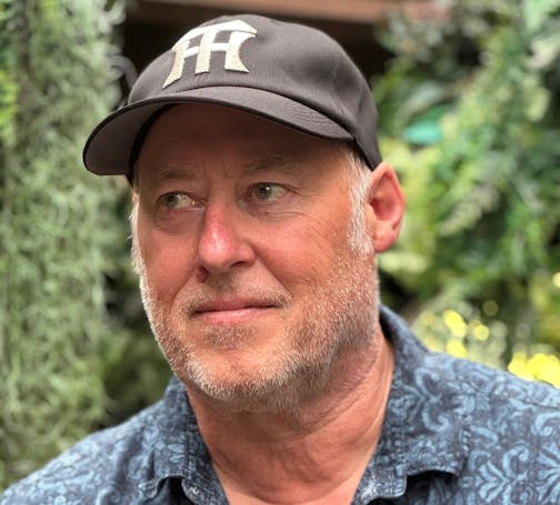 photo of author Stewart O'Nan in a baseball cap, in front of some greenery