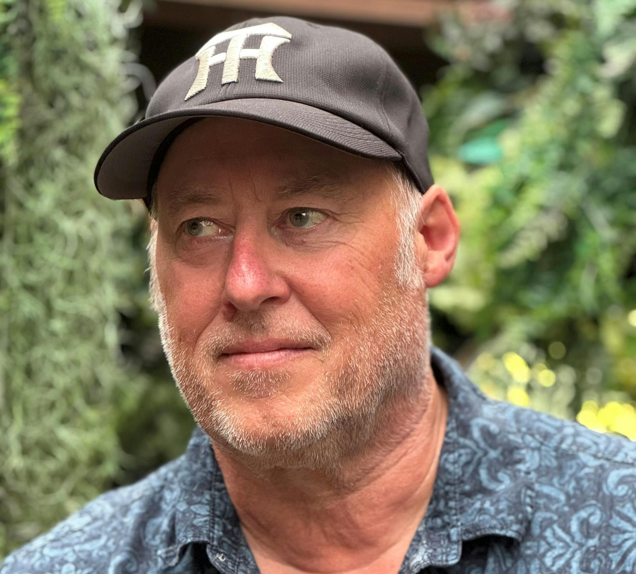 photo of author Stewart O'Nan in a baseball cap, in front of some greenery