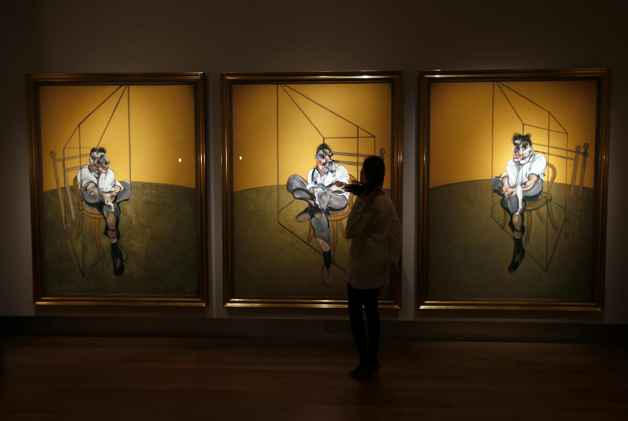 An auction house worker poses for the photographers in front of a Francis Bacon's oil on canvas triptych painting entitled 'Three Studies of Lucian Freud'', in central London, Monday, Oct. 14, 2013. The artwork will be offered in auction at Christie's New York 'Evening Sale of Post-War and Contemporary Art' on Nov. 12, 2013. (AP Photo/Lefteris Pitarakis) ORG XMIT: LLP103