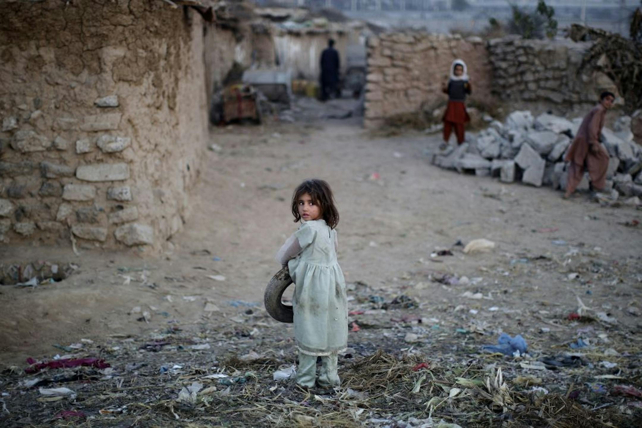 An Afghan refugee girl, looks back after picking up a tire from the ground, in a slum on the outskirts of Islamabad, Pakistan, on Nov. 26, 2012.