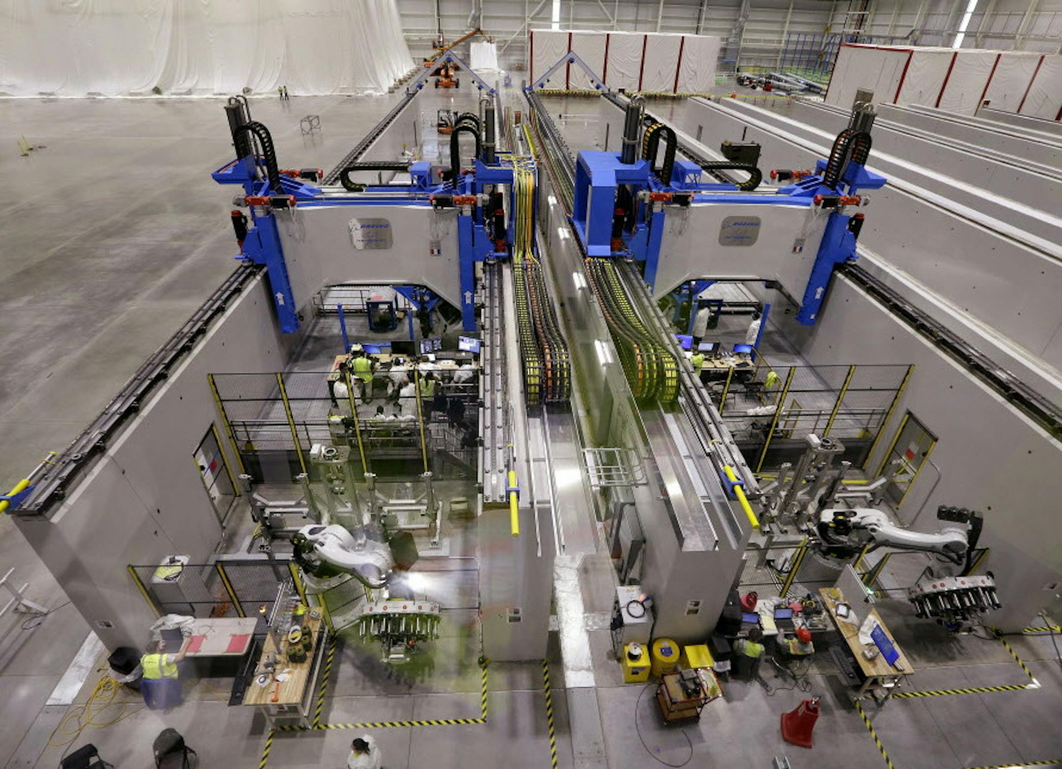 A gantry system where overhead supports hold robotic heads that will be used to build carbon fiber wings work through testing of the devices at the new Boeing 777X Composite Wing Center a day ahead of its grand opening, Thursday, May 19, 2016, in Everett, Wash. The facility, which is still under construction, will manufacture the world's largest composite wings for Boeing's newest commercial jetliner, the 777X. (AP Photo/Elaine Thompson)