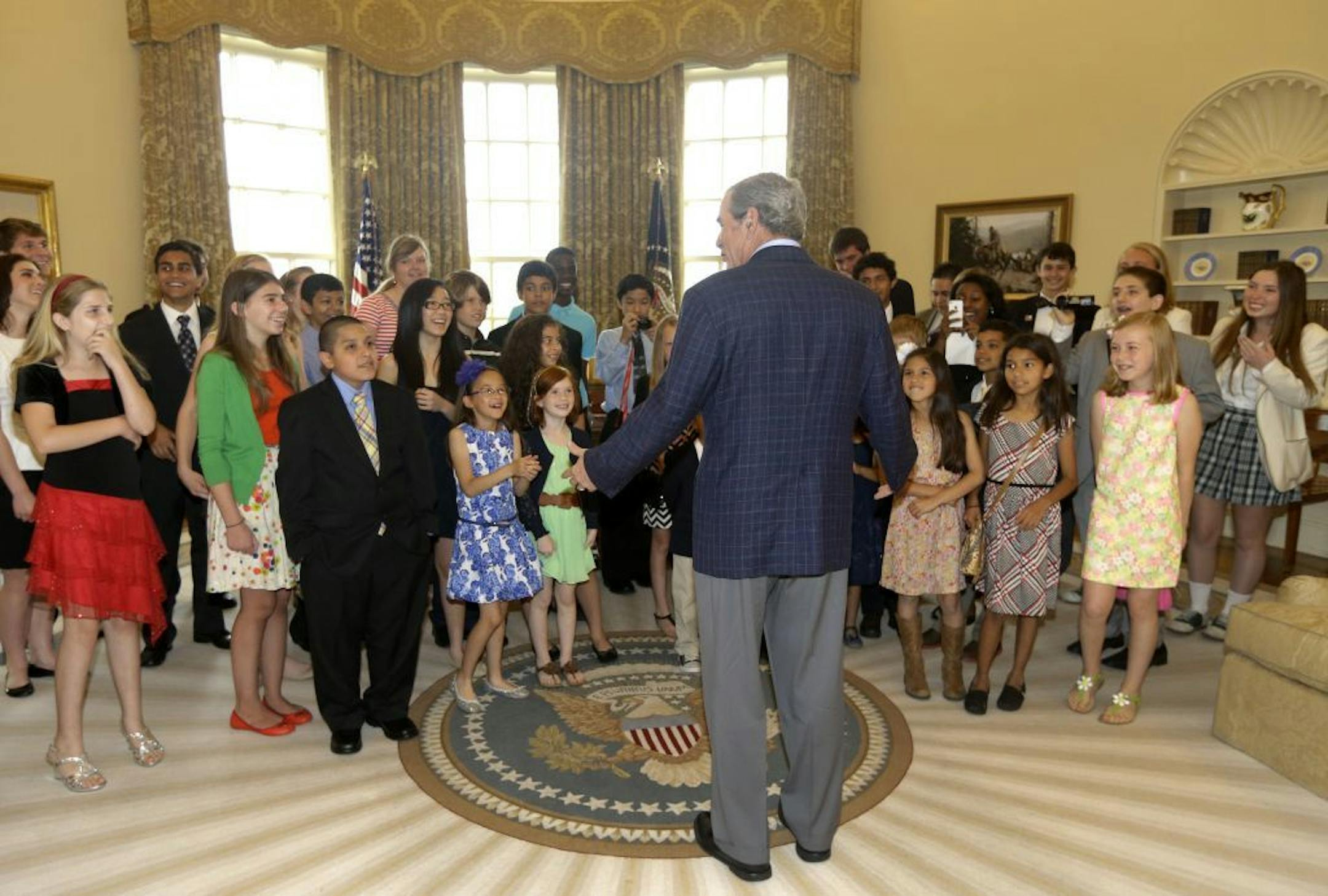 Former President George W. Bush, center, surprises 43 Dallas-Fort Worth area school children in the replica of the oval office at the Bush Presidential Library Wednesday, May 1, 2013, in Dallas. The students were the first official guest of the museum on its' opening day.