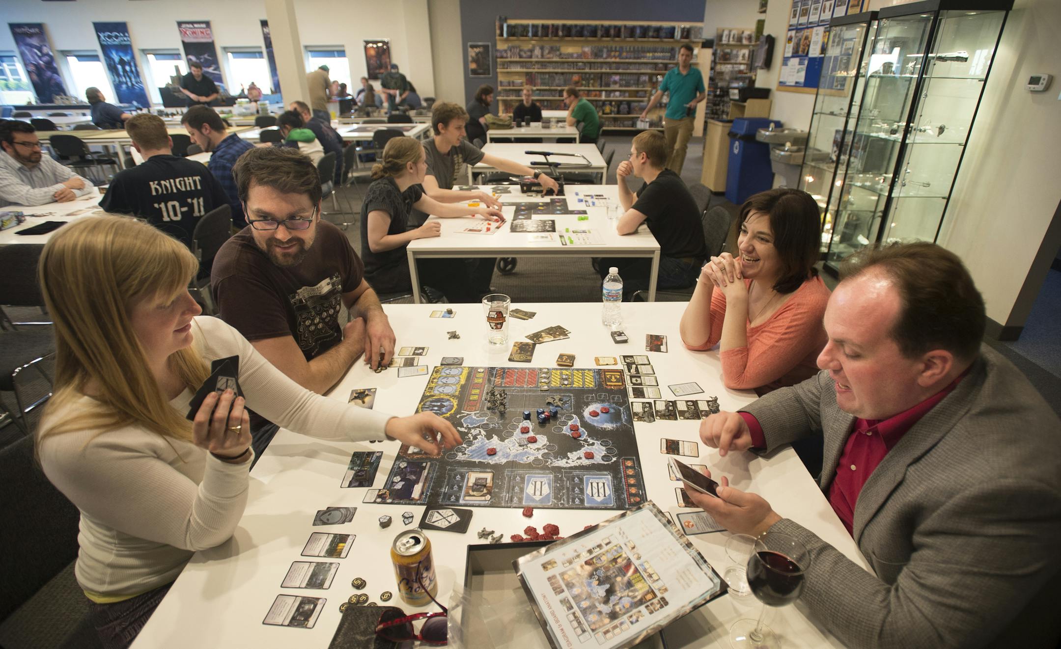Benjamin Fribley and Joanna Olson, left, play "XCOM: The Board Game" with Amanda Ressler and Emeric Dwyer on Friday night at Fantasy Flight. The game is a cooperative strategy and uses a cell phone app to drive the direction of the game. ] (Aaron Lavinsky | StarTribune) aaron.lavinsky@startribune.com Gaming company "Fantasy Flight" has a cafe and bar where gamers can come eat, drink and game and has become a home for the after-hours gaming community. Fantasy Flight was photographed Friday, April