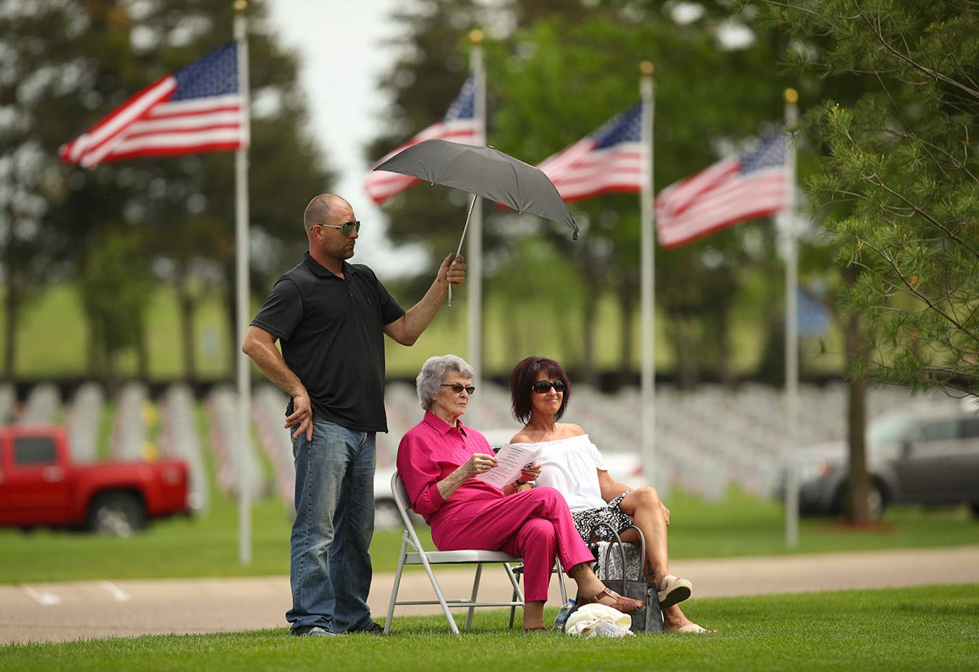 A man held an umbrella to shade two women attending the memorial program to honor veterans Sunday in Little Falls, Minn. Nearly 1000 people turned out for the even at the Minnesota State Veterans Cemetery.