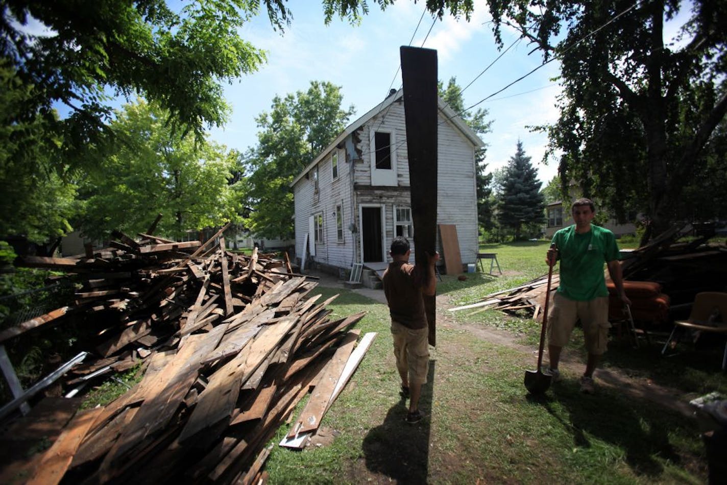 Project manager Andres Ariza carried an old board across the lawn to pull out old nails as he recycled the boards to reuse in the remodeling of a foreclosed home Thursday, August 4, 2011, in the Frogtown neighborhood of St. Paul, Minn. as part of the Frogtown Community House Project. At the right is volunteer Brian Schletty.