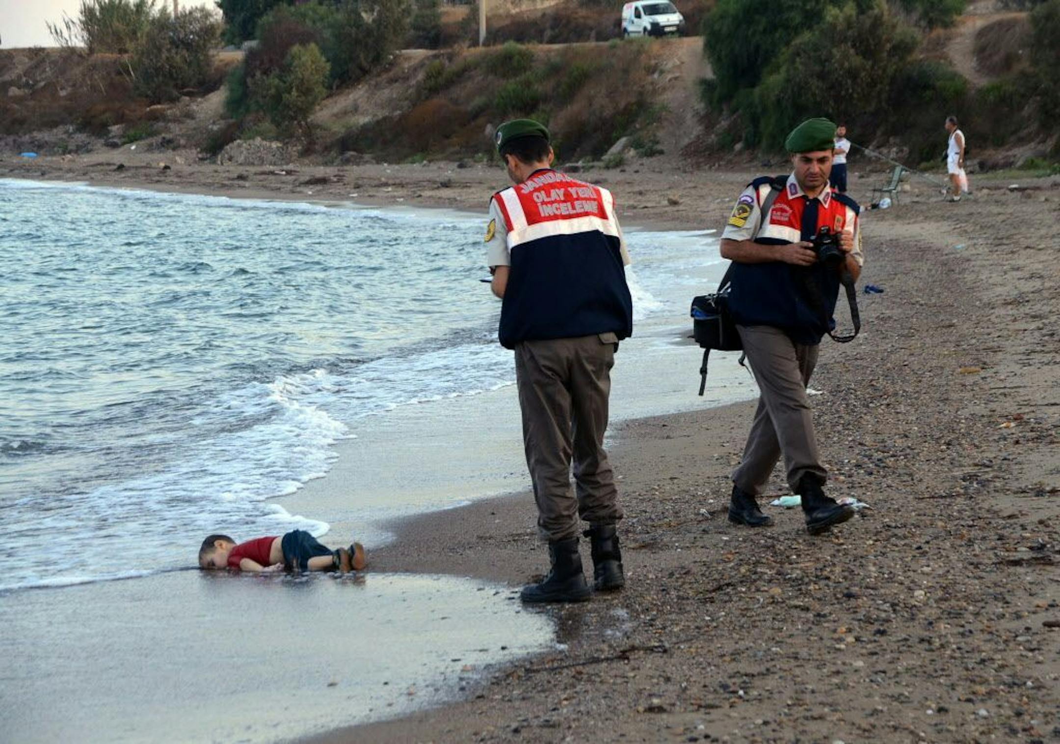 Paramilitary police officers investigate the scene before carrying the lifeless body of Aylan Kurdi, 3, after a number of migrants died after boats carrying them to the Greek island of Kos capsized.