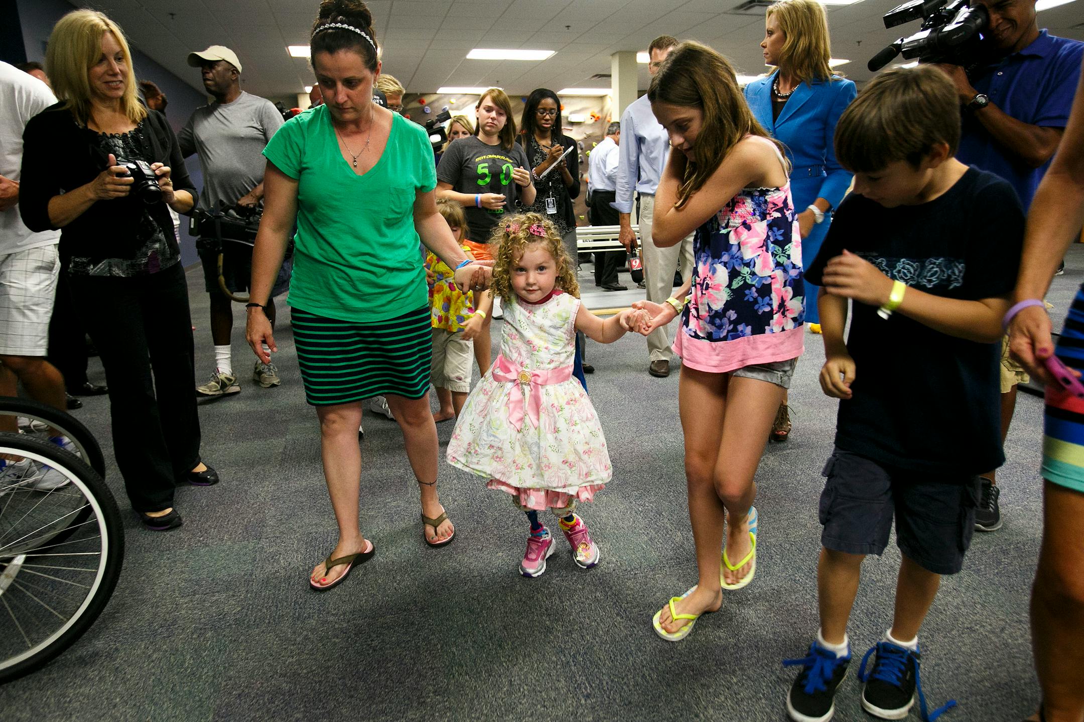 Ireland Nugent, 2, walks on her prosthetic legs while holding on to her mother, Nicole's, and sister, Italia Nesbitt, 11, right, hands at Prosthetic and Orthotic Associates in Orlando on Monday, June 17, 2013. Ireland Nugent lost both feet in a lawn mower accident.