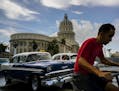 FILE - In this July 15, 2016 file photo, a man cycles alongside taxi drivers near the Capitol building in Havana, Cuba. A rare poll of Cuban public op