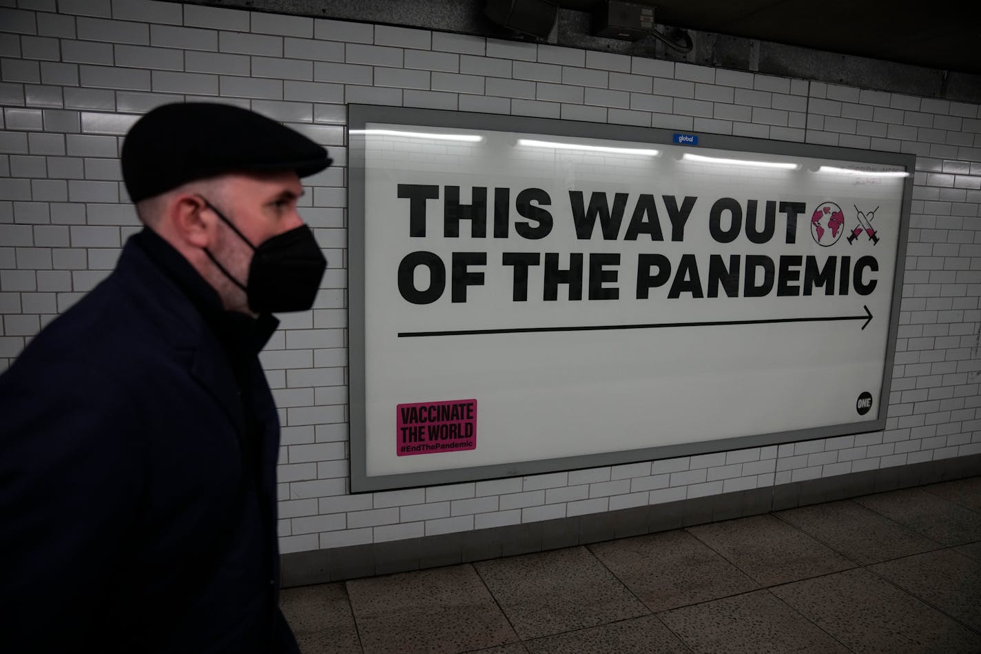 FILE - A man wearing a face mask to curb the spread of coronavirus walks past a health campaign poster from the One NGO, in an underpass leading to Westminster underground train station, in London, Thursday, Jan. 27, 2022. Scientists are warning the British government not to weaken the country's ability to monitor and track the coronavirus when Prime Minister Boris Johnson ends the requirement for people in England to self-isolate if they contract COVID-19. Johnson will announce details in Parliament on Monday, Feb. 21, 2022 of the government's plan for "living with COVID." (AP Photo/Matt Dunham, File)