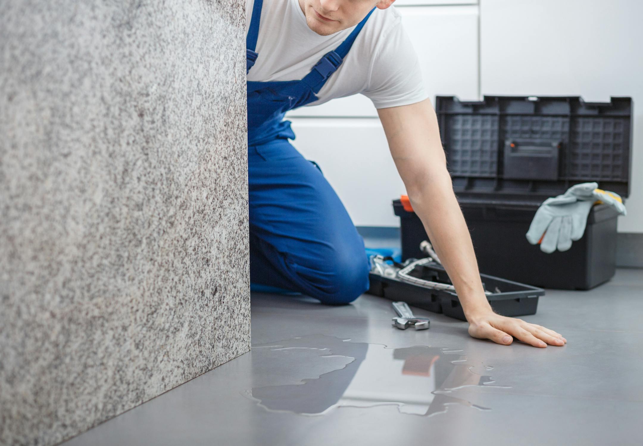 Plumber with toolbox looking at water on the floor from broken dishwasher
