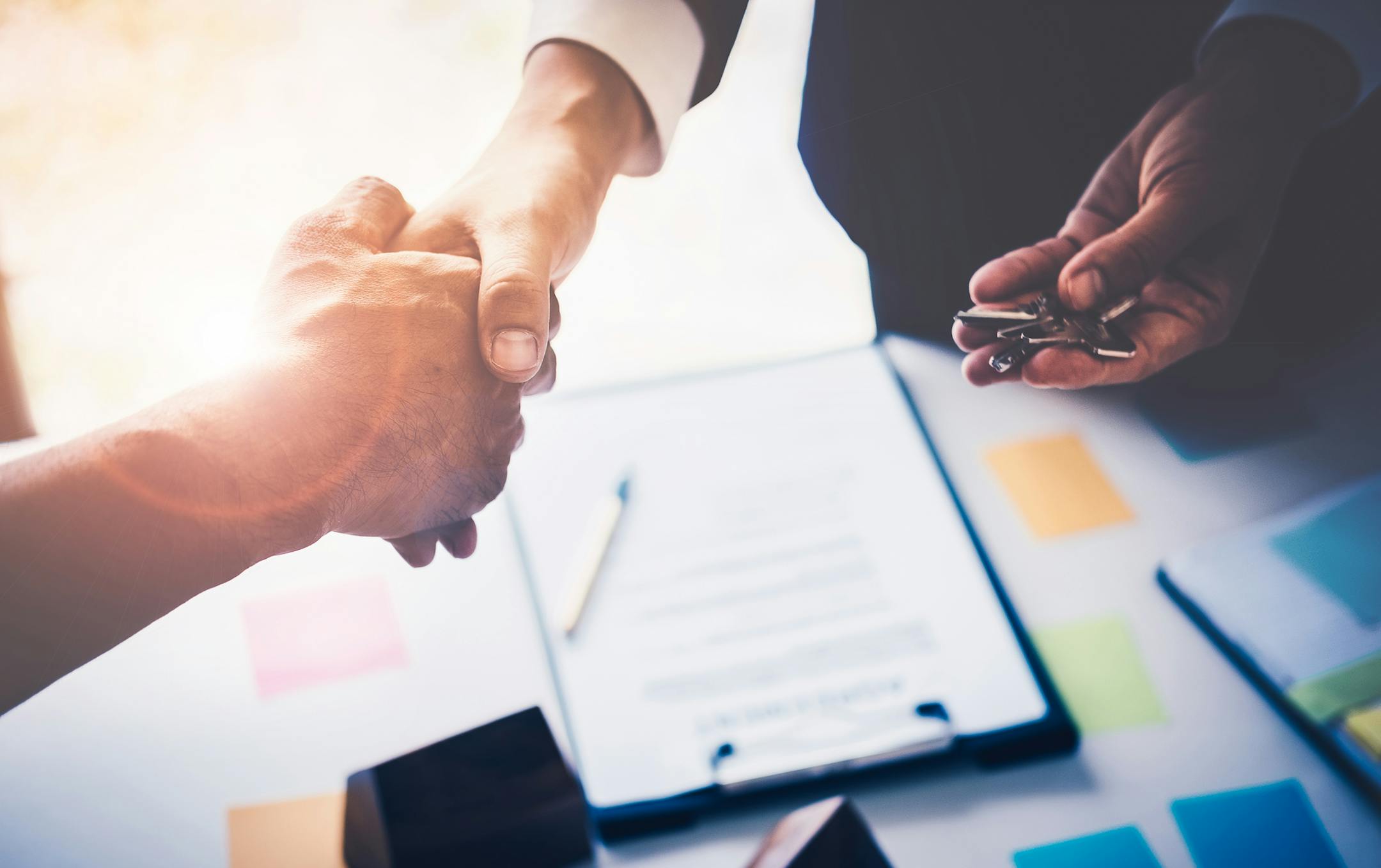 Agents are giving house keys of customer with handshaking after good deal at agency office. Real Estate and Agreement concept.