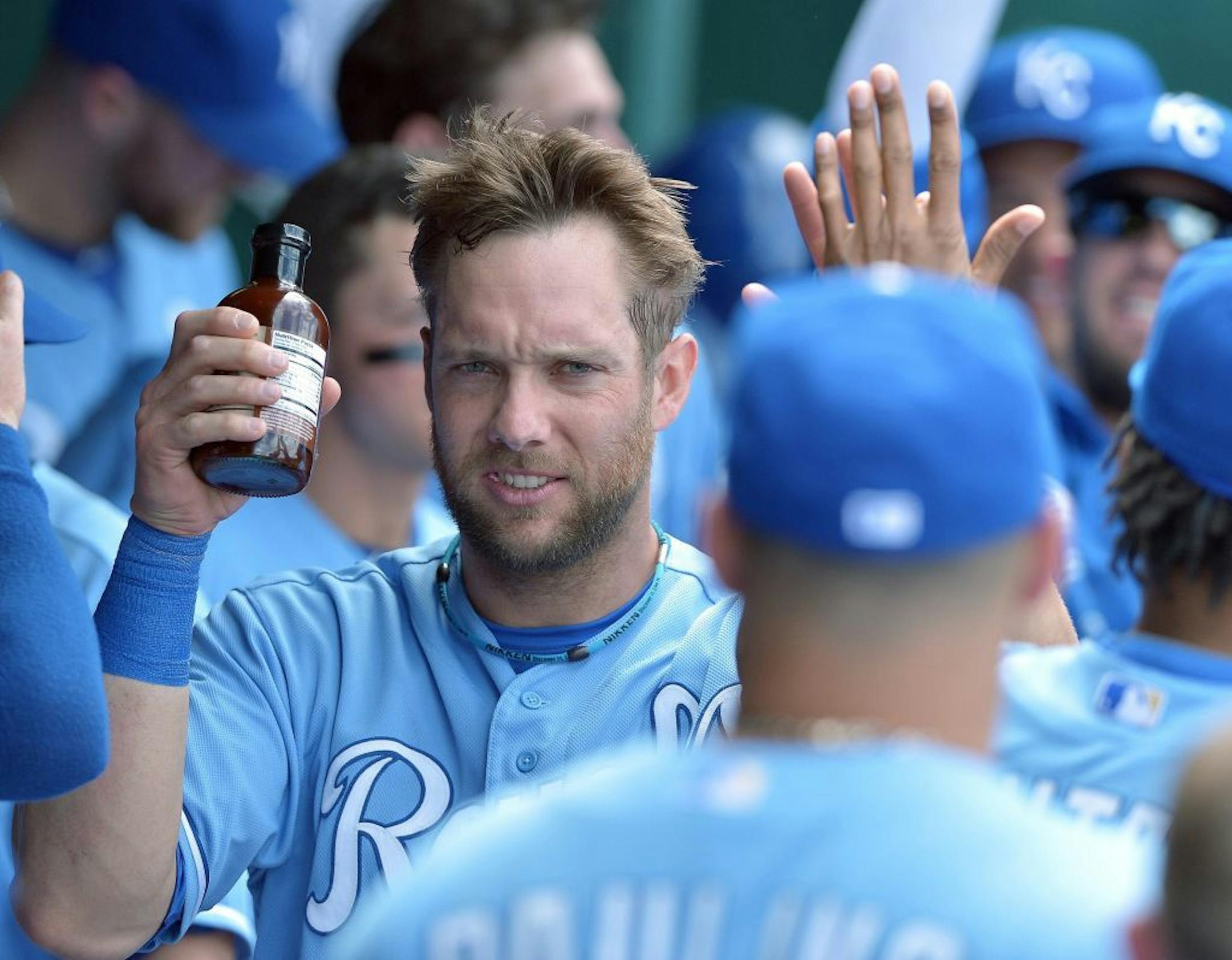 Carrying a bottle of Billy Butlers Hit a Ton Barbecue Sauce, Kansas City Royals' Alex Gordon (4) is congratulated by teammates in the dugout after scoring on a single by Eric Hosmer in the eighth inning at Kauffman Stadium in Kansas City, Missouri, Sunday, June 9, 2013.