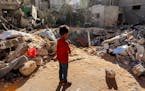 A boy stands before an impact crater at the site of a building that was hit by Israeli bombardment