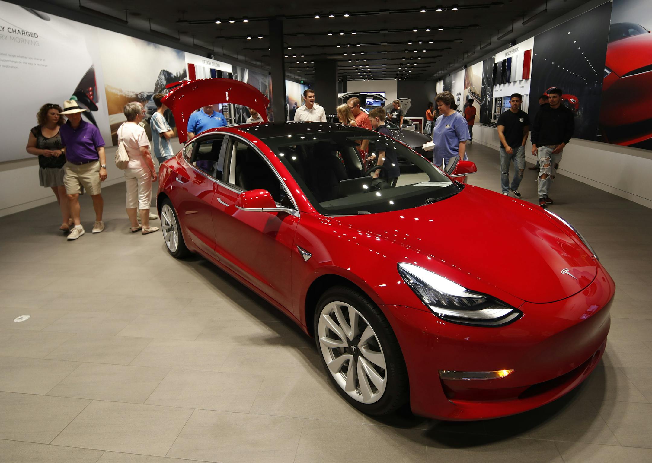 FILE- In this July 6, 2018, file photo, prospective customers confer with sales associates as a Model 3 sits on display in a Tesla showroom in the Cherry Creek Mall in Denver. Tesla is suffering one of its worst sell-offs of the year after announcing it would begin closing all of its stores in favor of selling its electric cars exclusively online. The goal is to allow Tesla to lower the price of its Model 3, the vehicle that CEO Elon Musk envisions as the company’s first mass-market vehic
