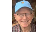An elderly man wearing a blue baseball cap looks at the camera and smiles.