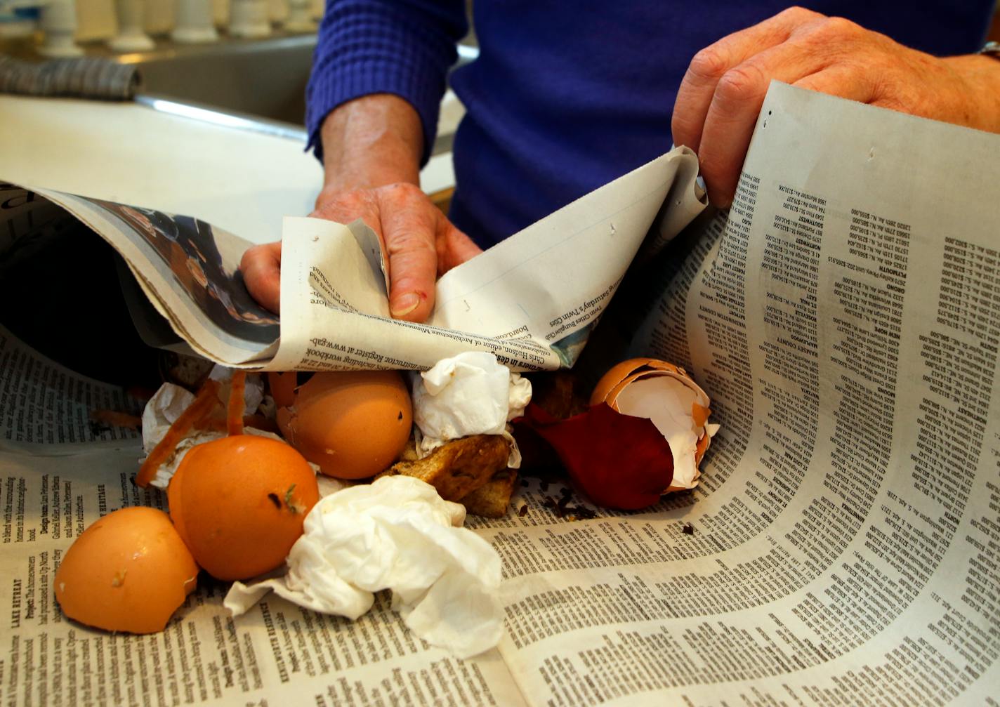 Dottie Dolezal wraps organic wastes into a newspaper in preparation for disposal.