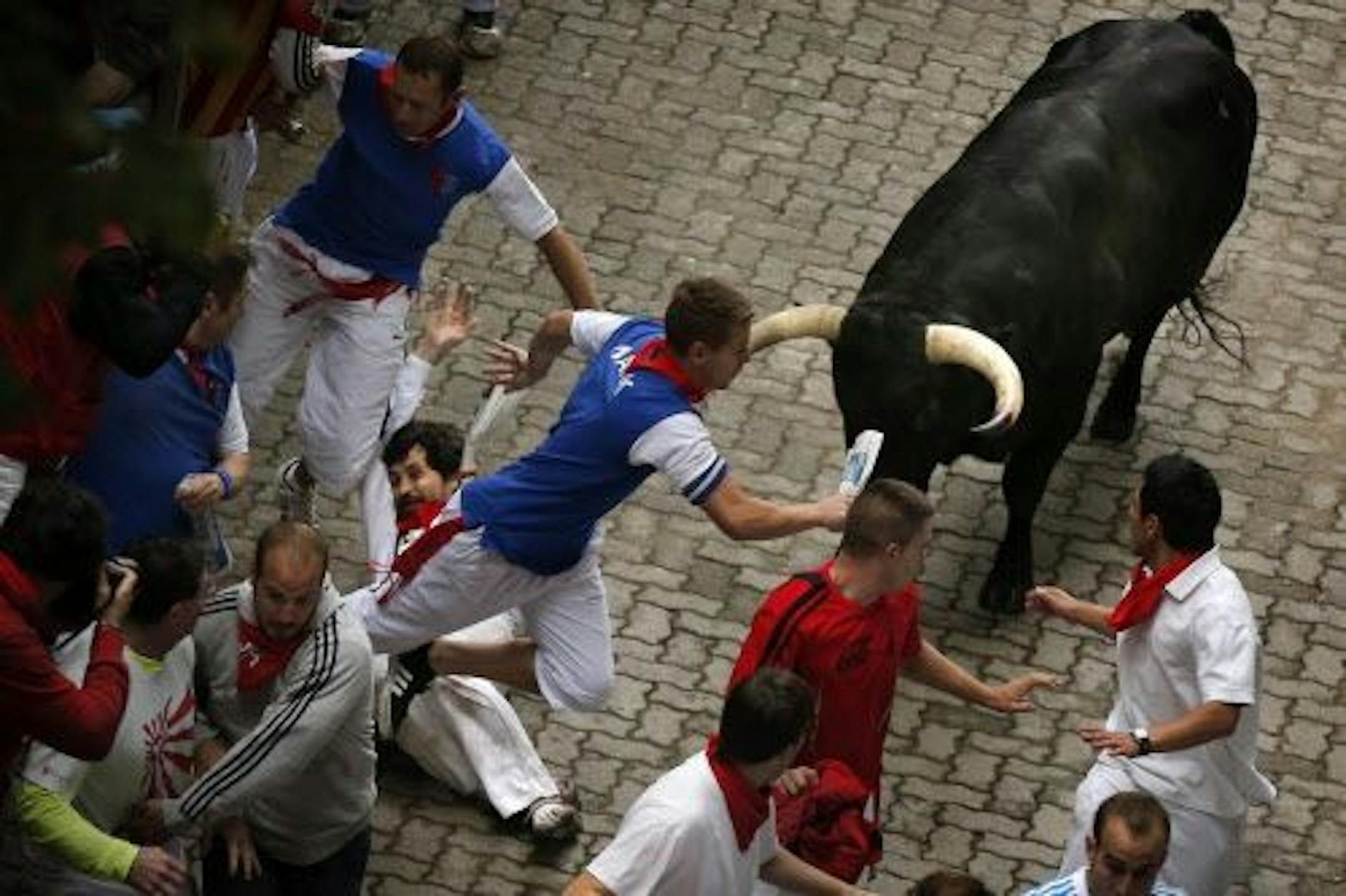 U.S. runner Bill Hillmann, 35, from Chicago, center left, falls seconds before a Victoriano del Rio ranch fighting bull gored him on his right leg during the running of the bulls of the San Fermin festival, in Pamplona, Spain, Wednesday, July 9, 2014.