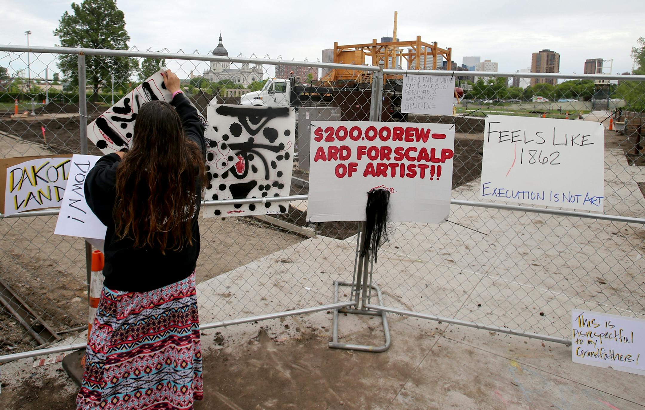 A controversial new sculpture at the Walker Art Center that prompted an outcry among Minnesota's American Indian communities will be dismantled, the director said Saturday. Here, a woman hangs up a protest sign on a construction fence near the controversial new sculpture at the Walker Sculpture Garden Saturday, May 27, 2017, in Minneapolis, MN.