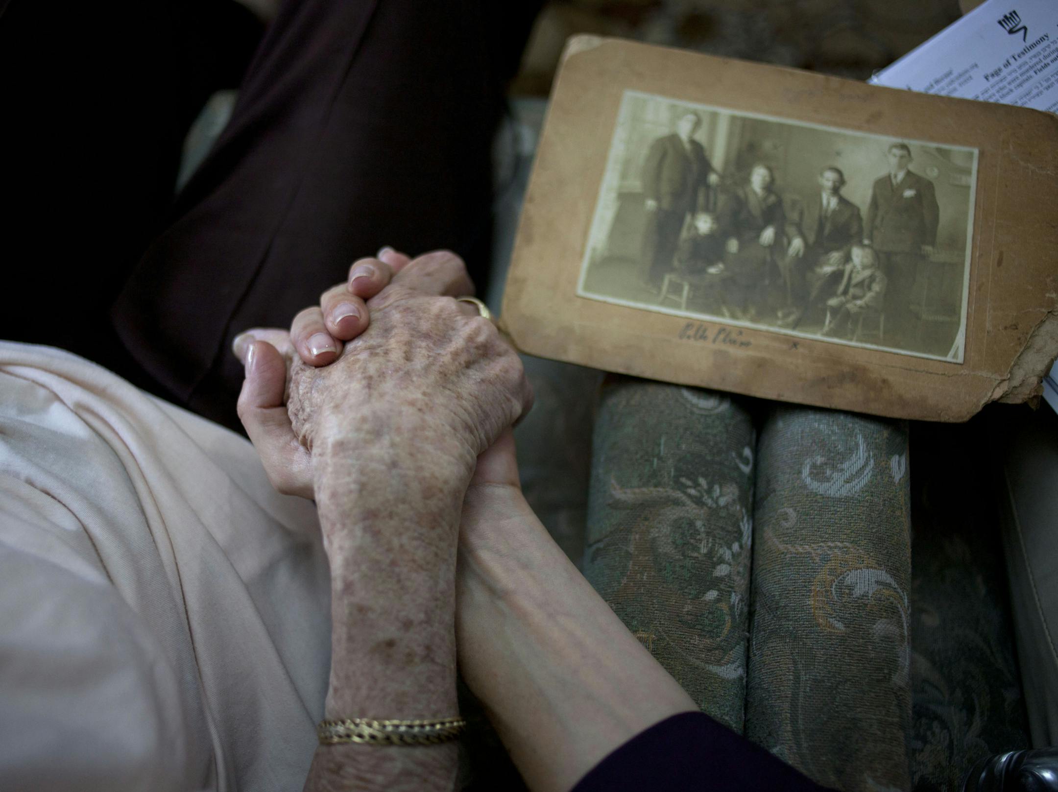 In this photo taken on Sunday, May 5, 2013, Holocaust survivor Rivka Fringeru, 82, left, holds hand with Cynthia Wroclawski, director of Yad Vashem names collection project as they sit in her living room in Rehovot, central Israel. With a hand on her chest and moistness building in her eyes, 82-year-old Rivka Fringeru battled back tears as she reeled off a list of names she has rarely voiced in the past 70 years. First her father, Moshe, then her mother, Hava, and finally her two older brothers,