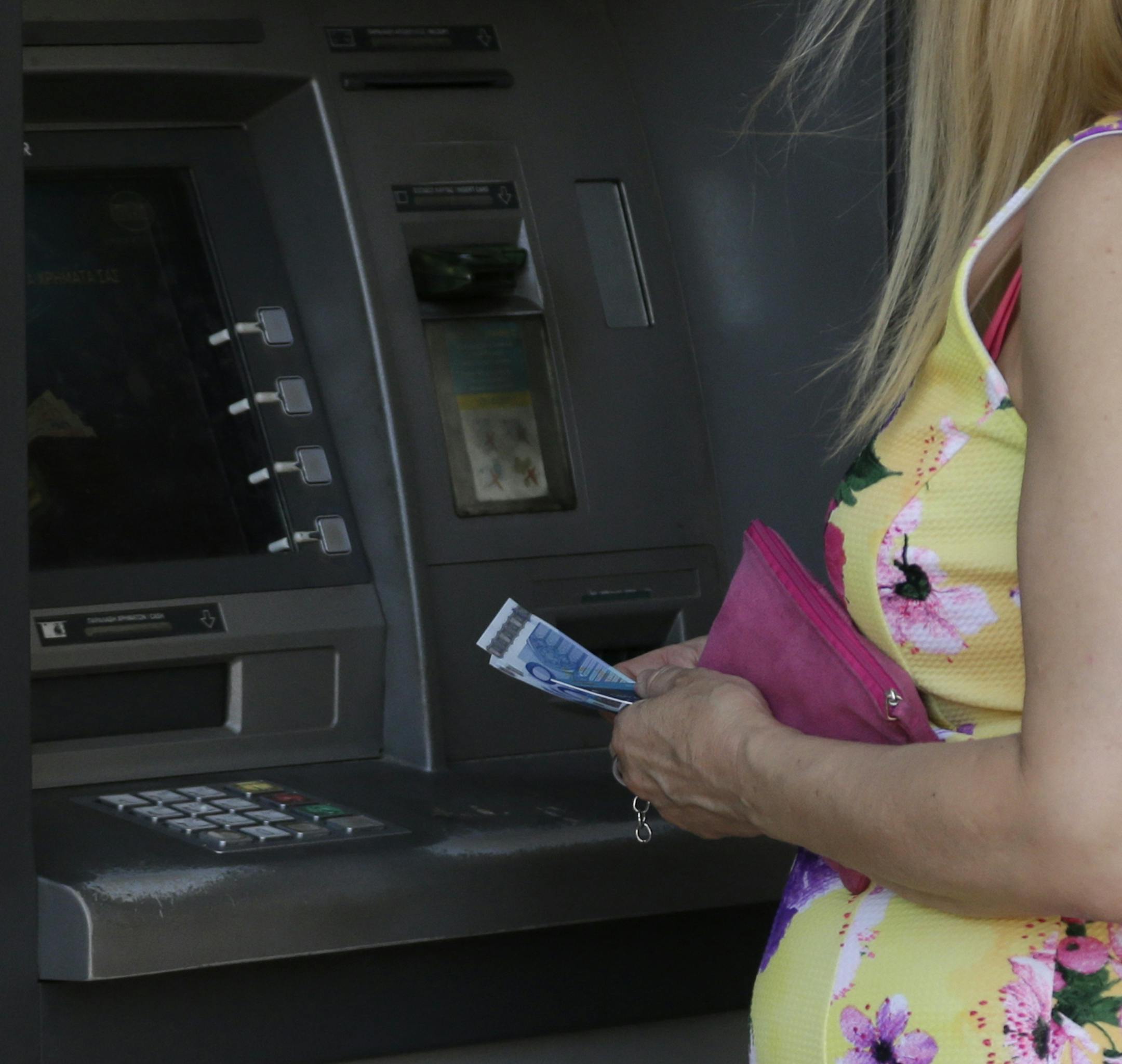 A woman uses an ATM of a bank after the government's decision last week to limit daily cash withdrawals to 60 euro ($66) in Athens, Tuesday, July 7, 2015. Greek Prime Minister Alexis Tsipras was heading Tuesday to Brussels for an emergency meeting of eurozone leaders, where he will try to use a resounding referendum victory to eke out concessions from European creditors over a bailout for the crisis-ridden country. (AP Photo/Petr David Josek) ORG XMIT: ATH107