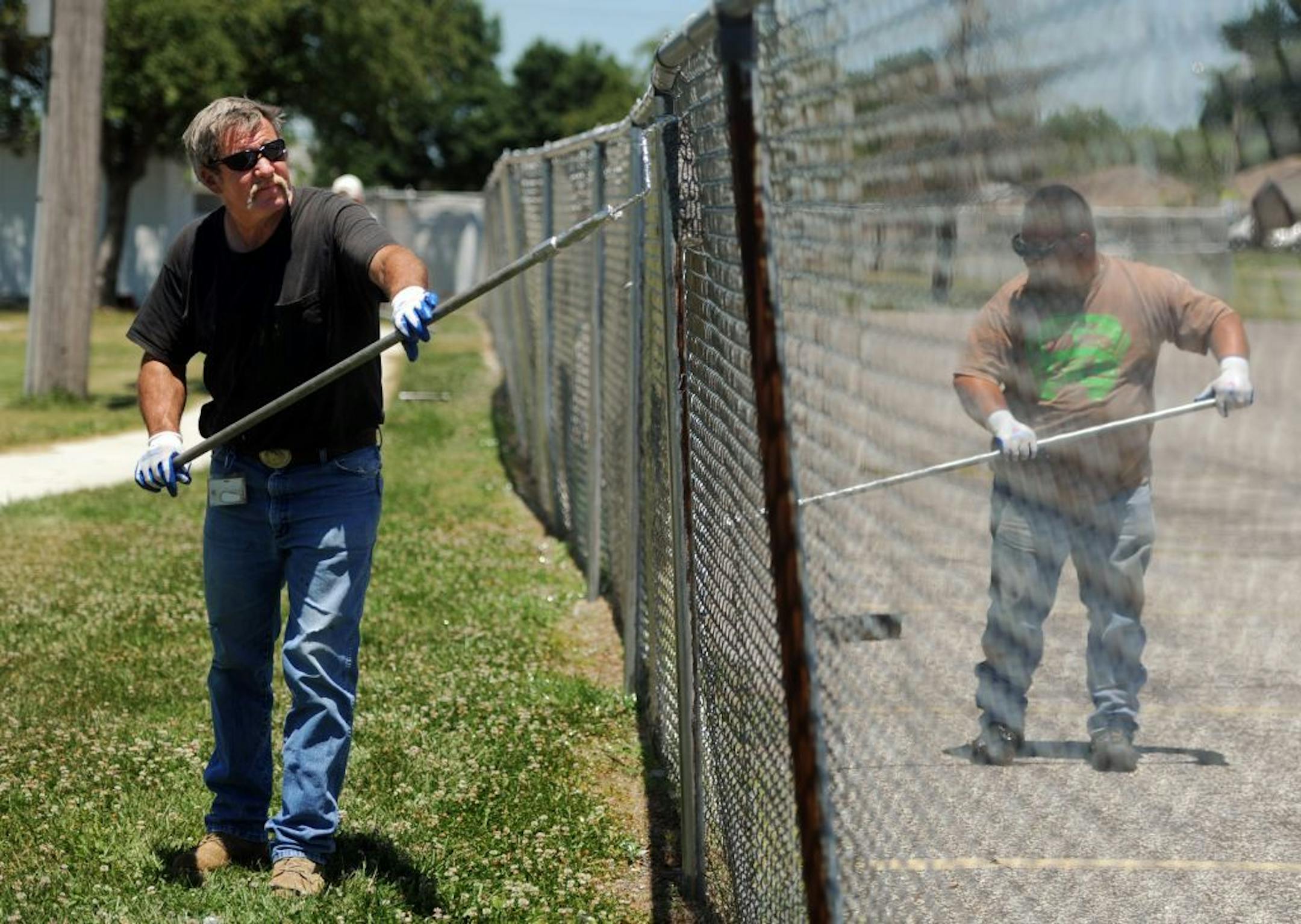 FILE - In this June 26, 2012, file photo, Dave Morton, left, and Brian Goodman, who both drive school buses for Daviess County Public Schools during the school year, coat the fence around Apollo High School's soccer field with metallic silver paint. Morton said they both took the temporary job with DCPS's maintenance department to earn a little extra money over the summer.