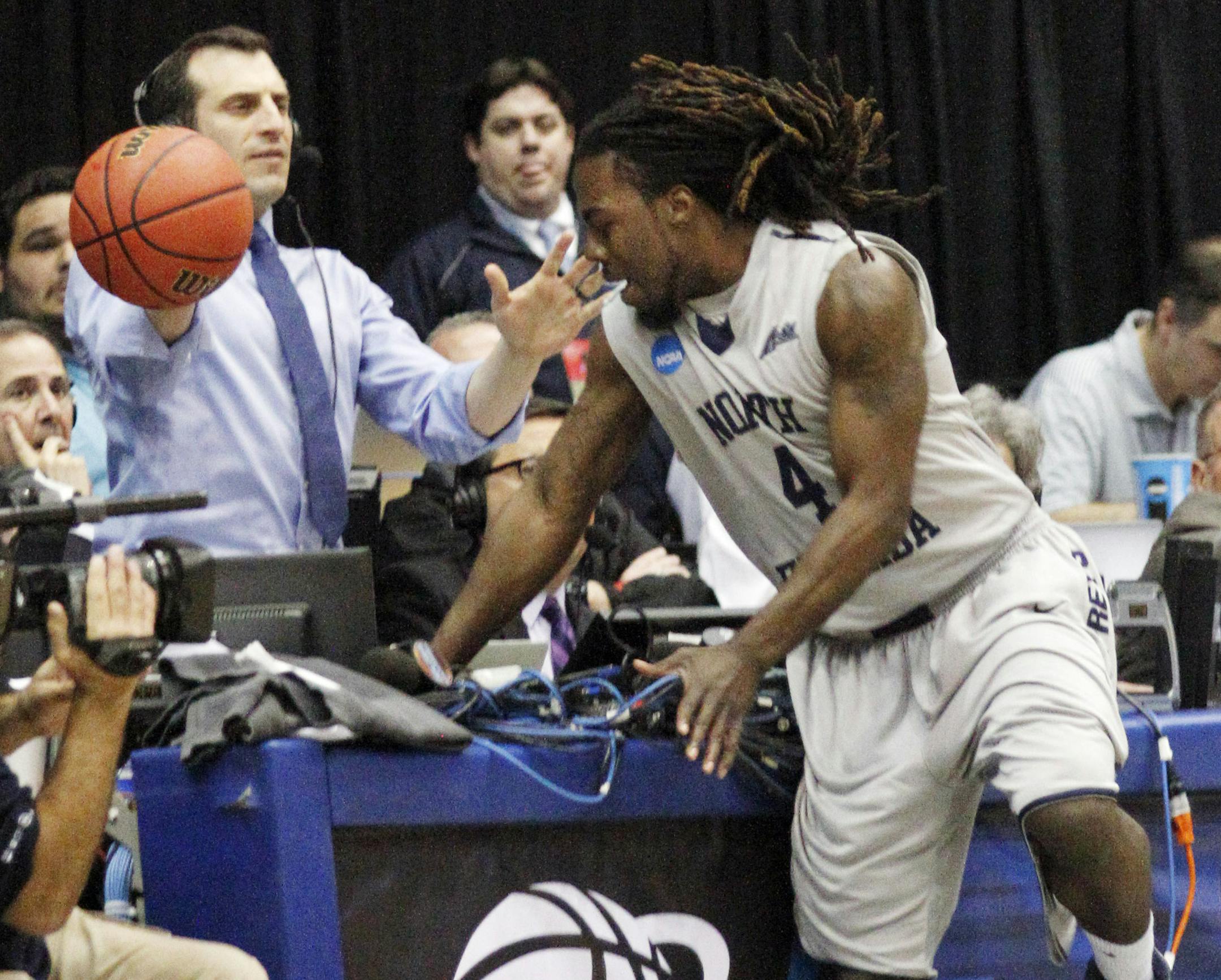 North Florida's Devin Wilson (4) crashes into the broadcast table chasing the ball in the first half of a first-round NCAA tournament basketball game against Robert Morris, Wednesday, March 18, 2015, in Dayton, Ohio. (AP Photo/Skip Peterson)