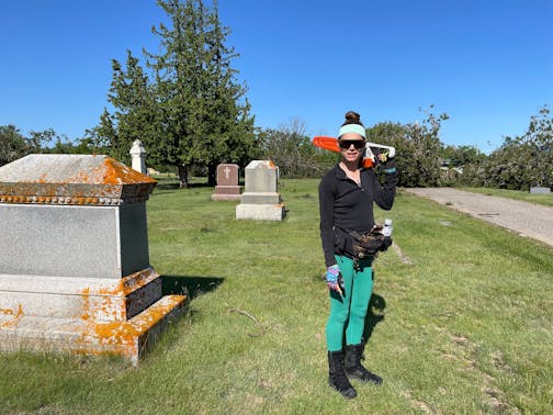 woman standing holding chain saw next to large grave marker