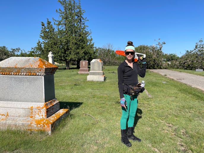 woman standing holding chain saw next to large grave marker