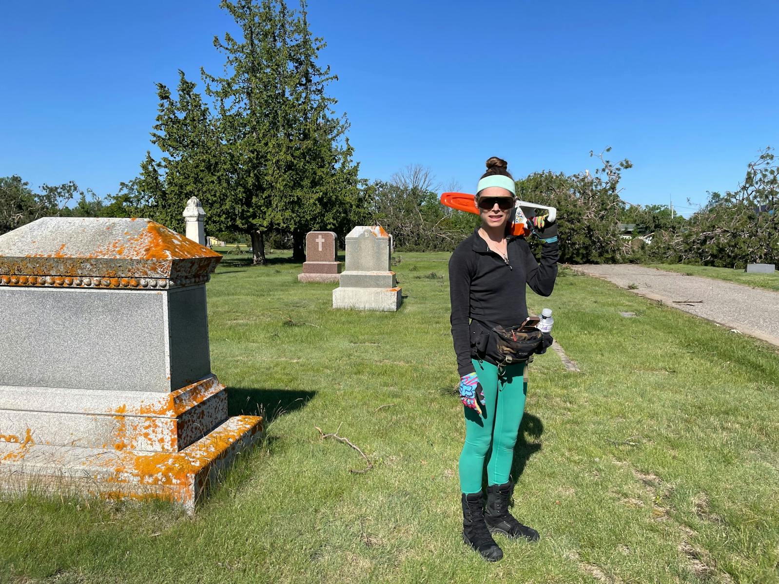 woman standing holding chain saw next to large grave marker