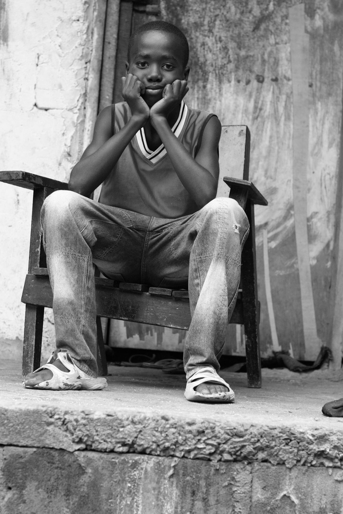 "A 13-year-old boy from Liberia, West Africa, sitting sadly in a chair, with his chin in his hands."