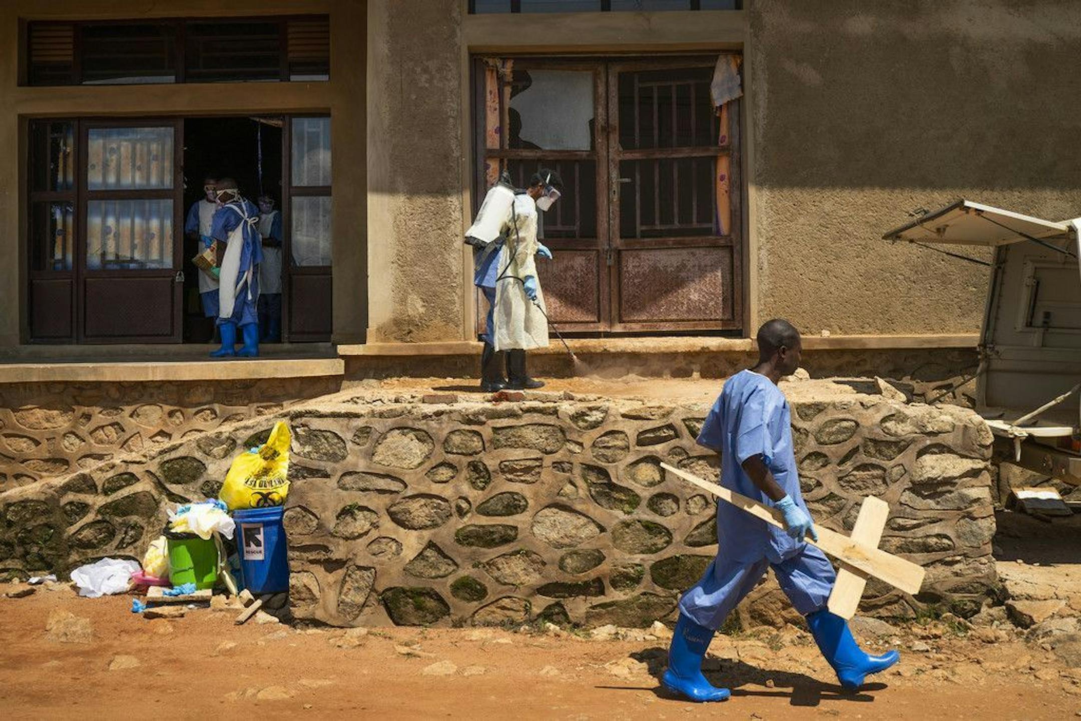 In this photograph taken Sunday July 14, 2019, a morgue employee walks with a cross past others disinfecting the entrance to the morgue in Beni, Congo DRC. The head of the World Health Organization is convening a meeting of experts Wednesday July 17, 2019 to decide whether the Ebola outbreak should be declared an international emergency after spreading to eastern Congo's biggest city, Goma, this week. More than 1,600 people in eastern Congo have died as the virus has spread in areas too dangerou