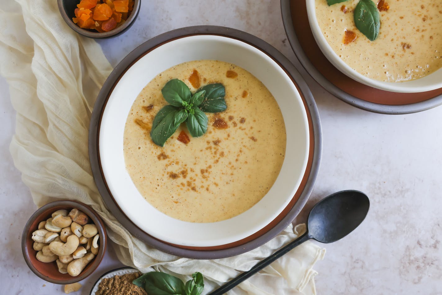 A bowl of savory creamy peach and apricot soup that's topped with cashews and basil leaves.