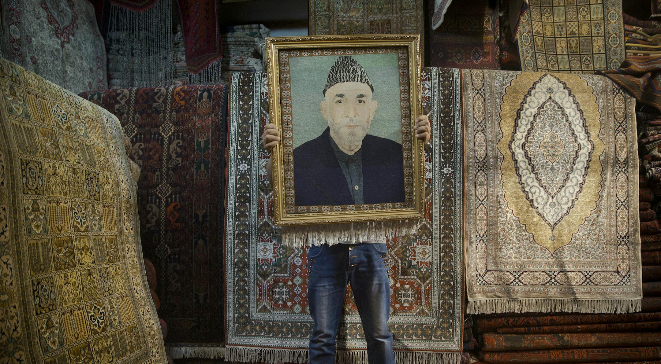 An Afghan carpet seller holds up a framed carpet depicting Afghan President Hamid Karzai in his store in Kabul, Afghanistan, Sunday, March 30, 2014. Afghans go to the polls April 5, 2014 to choose a new president, and that in itself may one day be considered Karzai’s greatest achievement. (AP Photo/Anja Niedringhaus)