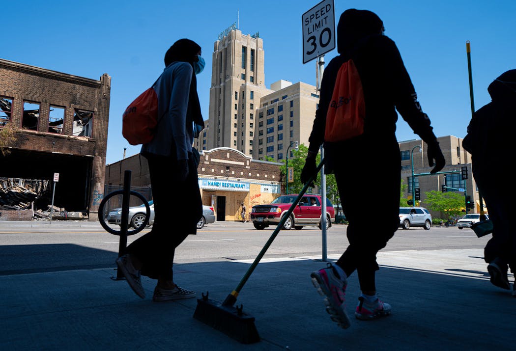 Broom-wielding volunteers walked up and down E. Lake Street on June 3, helping with the clean up. Behind them are the burned-out Foot Locker store, looted Hamdi Restaurant and Midtown Global Market, which had broken windows.