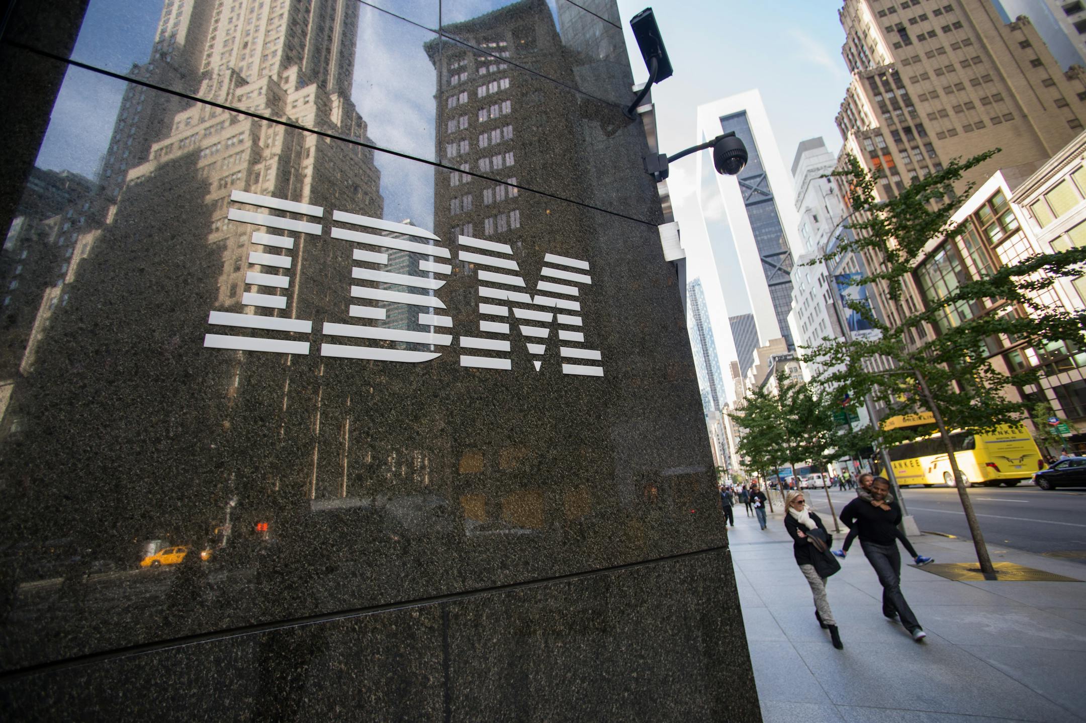 Pedestrians walk past an International Business Machines Corp. (IBM) logo that is displayed in front of the company's offices in New York, U.S., on Monday, Oct. 14, 2013. International Business Machines is scheduled to report 3Q results post-market tomorrow. Photographer: Craig Warga/Bloomberg