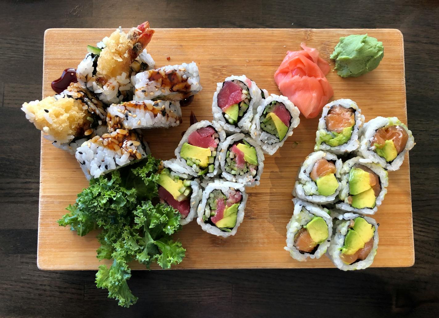 Three sushi rolls on a wooden board, garnished with pickled ginger and wasabi.